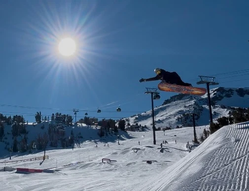 Rider airborne above a snowy slope beneath the bright sun