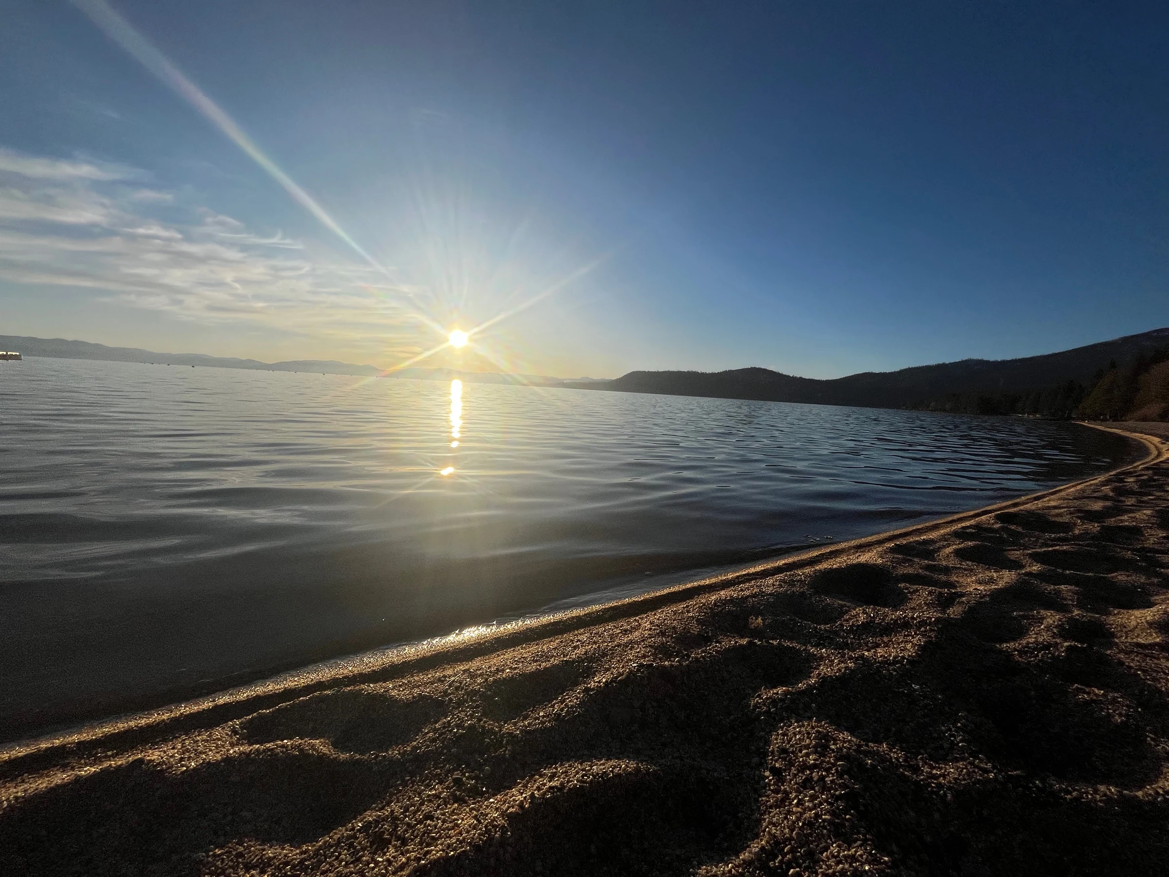 Sunlight reflected across calm water beside a sandy shore