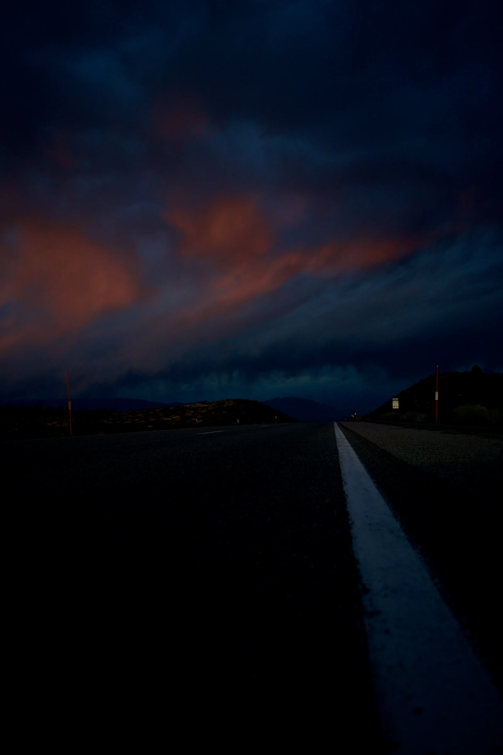 Empty road leading toward mountains under a dark sunset